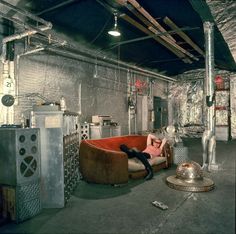 a woman sitting on a red couch in a room with exposed ceilings and metal pipes