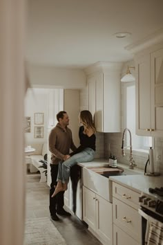 a man and woman standing in a kitchen next to each other looking at each other