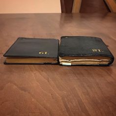 two black books sitting on top of a wooden table next to each other, one opened and the other closed