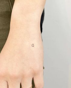 a woman's left hand with a small tattoo on the middle finger and an initial