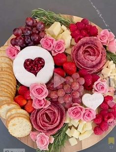 a platter with cheese, crackers and fruit arranged in the shape of a heart