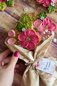 decorated cookies with pink and green flowers are on a table next to a hand holding a bag