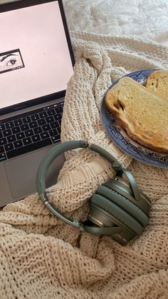 a laptop computer sitting on top of a bed next to headphones and a sandwich