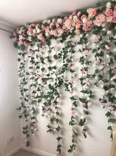 the wall is covered with pink flowers and greenery hanging from it's sides