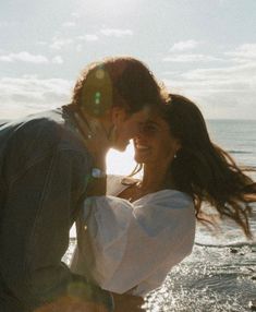 a man and woman kissing on the beach in front of the ocean with sun flares