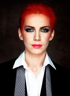 a woman with red hair and blue eyes wearing a black jacket, white shirt and tie