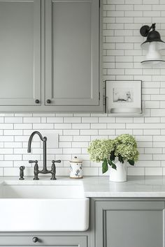 a kitchen with gray cabinets and white subway tile backsplash, black faucet