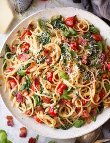 a plate of pasta with tomatoes, spinach and parmesan cheese on the side