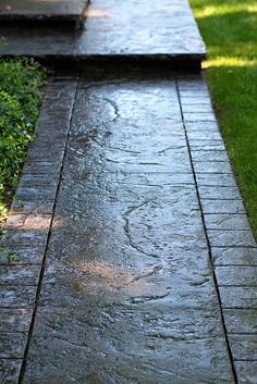 the sidewalk is wet and has water coming from it, as well as green grass