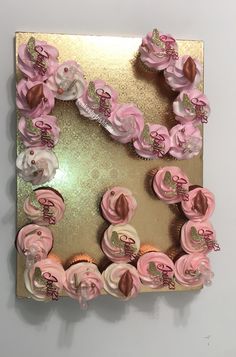 pink cupcakes are arranged in the shape of a letter on a gold background