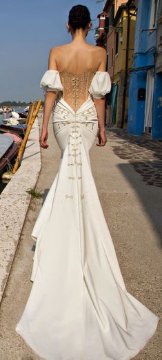 the back of a woman's dress as she walks down a street next to boats