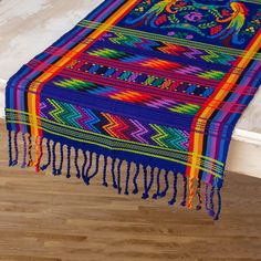 a multicolored blanket with tassels and fringe on the floor next to a bed