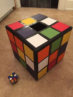 a rubik cube sitting on the floor next to a remote control device and an object that looks like it has been made out of colored squares