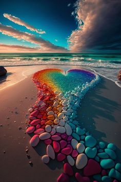 a rainbow heart made out of rocks on the beach with water and clouds in the background