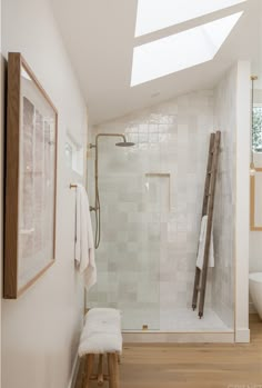 a white bathroom with a skylight above the shower and wooden stool in front of it