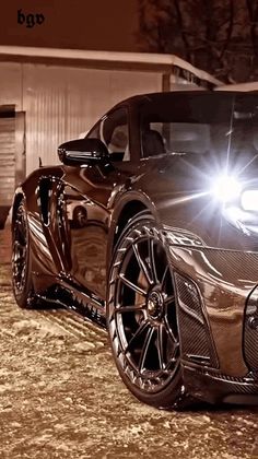 a brown sports car parked in front of a building at night with the headlights on