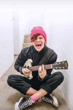 a young man sitting on the ground with an electric guitar in his hand and laughing