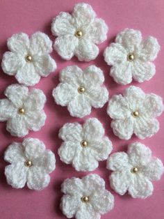 white crocheted flowers with gold centers on a pink background, ready to be sewn