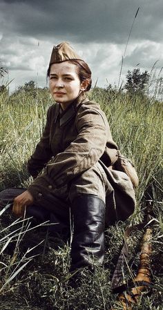 a woman sitting on the ground in tall grass with her head turned to the side