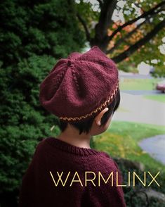 a young boy wearing a maroon sweater and hat looking out over a park with trees in the background