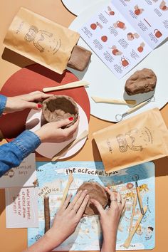 two hands are decorating a cake with chocolate icing and other decorations on the table