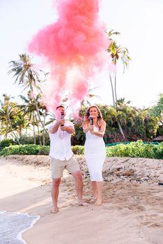 a man and woman standing on top of a sandy beach holding wine glasses in front of them