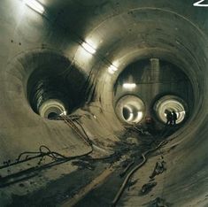 the inside of a large metal pipe with pipes running through it and two men standing in the middle