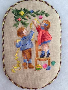 a cross stitched picture of two children playing with a toy on a white surface