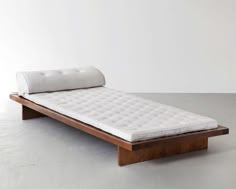 a white mattress sitting on top of a wooden bed frame in an empty room with concrete flooring