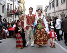 a man and woman dressed in traditional costumes walking down the street with their son on his arm