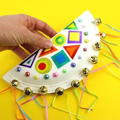 a hand is holding a paper plate with buttons and beads on it that has a rocket ship design