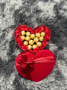 a heart shaped box filled with chocolates on top of a gray blanket next to a red bow