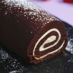 a chocolate roll covered in powdered sugar sitting on top of a black plate next to strawberries