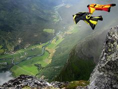 a man in yellow and black suit parachuting over a mountain range with green valley below