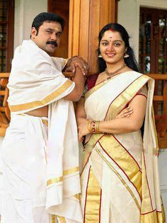 two people standing next to each other wearing white and yellow sari dresses with gold trims