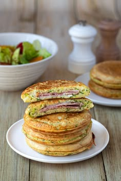 a stack of pancakes sitting on top of a white plate next to a bowl of salad