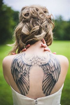 the back of a woman's neck with an angel tattoo on her upper half