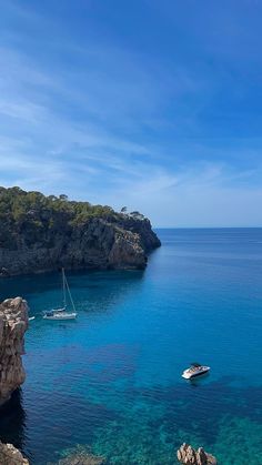 two boats floating in the blue water near some rocks and cliffs on a sunny day