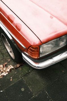 an old red car is parked on the side of the road with leaves all over it