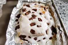 a piece of cake sitting on top of tin foil covered in white frosting and chocolate chips