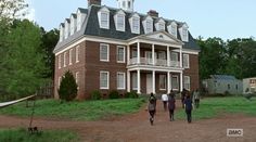 people walking in front of a large brick building on a dirt road next to trees