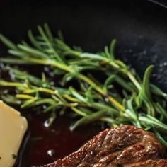 steak with gravy and butter in a skillet next to some green vegetables