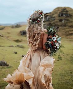 a woman with flowers in her hair is walking through the grass wearing a dress and holding a bouquet