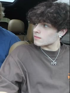 two young men sitting in the back seat of a car, one is wearing a necklace