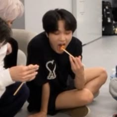 three people sitting on the floor eating food with chopsticks in their mouths,