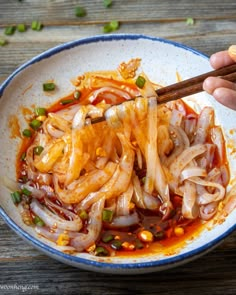 someone holding chopsticks over a bowl of food with onions and sauce on it