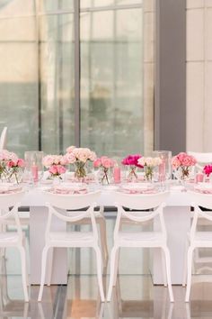 the table is set with pink and white flowers in vases, plates and glasses