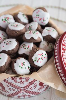 a bowl filled with cookies covered in white frosting and sprinkles next to a red tin