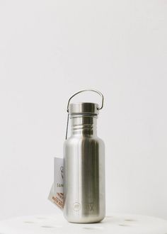 a stainless steel water bottle sitting on top of a white table next to a tag