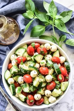 a white bowl filled with cucumber, tomatoes and basil on top of a blue towel